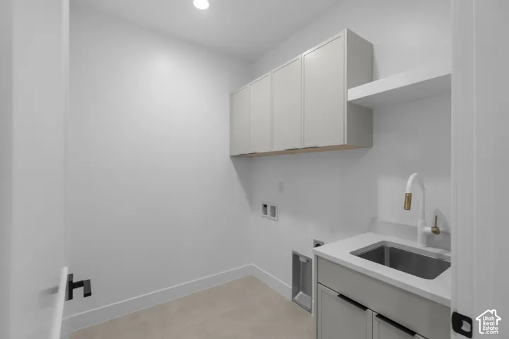 Modern laundry room featuring white cabinetry with ample storage, stainless steel utility sink with single-handle faucet, polished concrete flooring, and recessed ceiling lighting