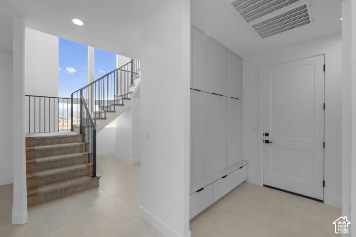 Staircase with wrought iron railing, tile flooring, built-in storage cabinetry, and a solid core entry door with black hardware