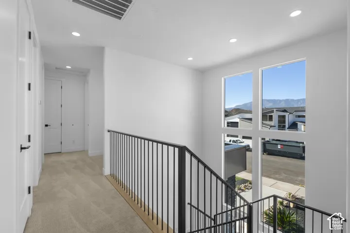 Two-story window wall, wrought iron railing, recessed lighting, neutral carpeting, and white interior doors