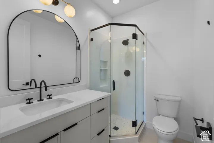 White vanity with black hardware, white countertop, black fixtures, and a corner glass-enclosed shower with black trim