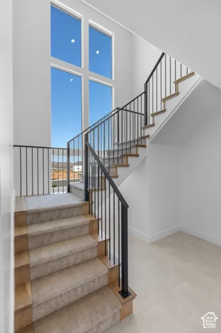 Two-story window wall, wood-finish stairs with carpet runners, black metal balusters, and light-toned floor tile