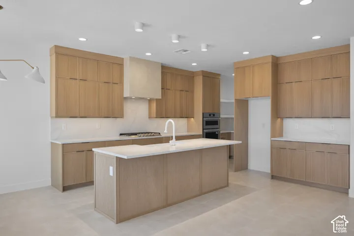 Modern kitchen featuring light wood-finish cabinetry, white countertops, a central island with an integrated sink, and recessed lighting