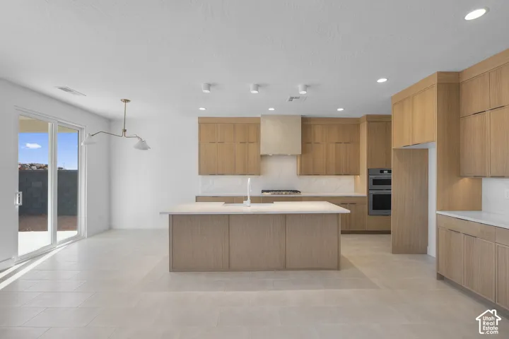 Contemporary kitchen featuring light wood-finish cabinetry, a central island with an integrated sink, and white countertops