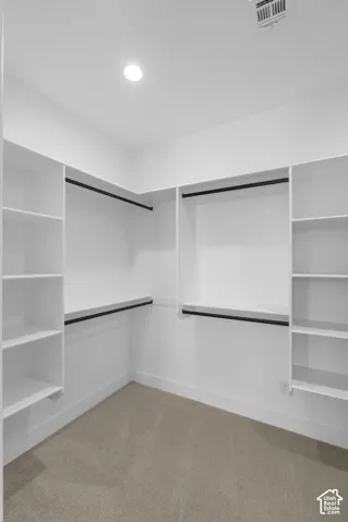 Built-in white shelving, black hanging rods, recessed ceiling lighting, and neutral carpet flooring
