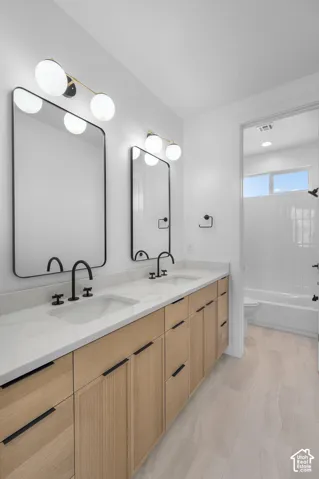 Spa-inspired primary bathroom featuring dual vanities with wood-finish cabinetry, white quartz countertops, and matte black faucetry