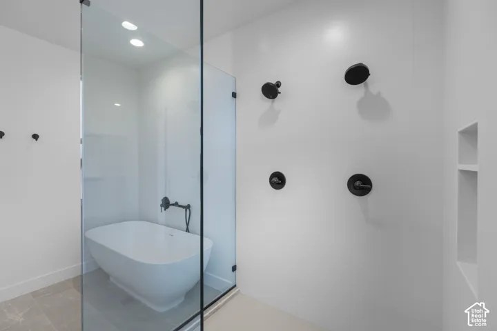 Frameless glass shower enclosure with a freestanding soaking tub, multi-head shower system, recessed lighting, and a built-in shower niche