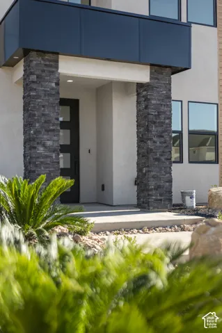 Modern entry featuring stacked stone columns, a contemporary black door with frosted glass panels, and an overhead architectural element