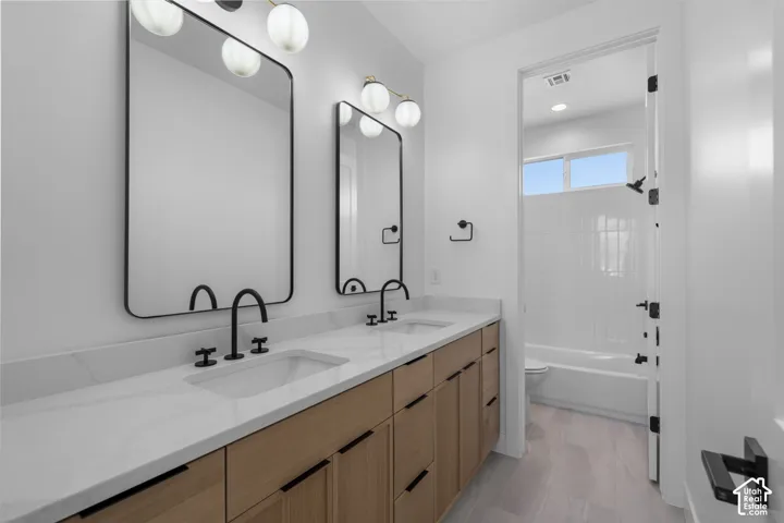 Spa-inspired primary bathroom featuring dual vanities with wood-finish cabinetry, white quartz countertops, and matte black fixtures