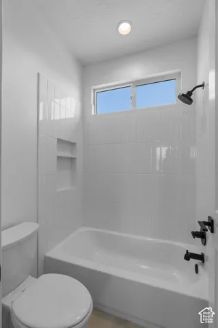 Bathtub with subway tile surround, matte black fixtures, recessed shower niche, and high window