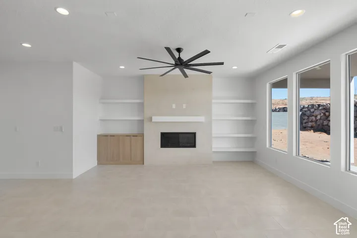 Spacious room featuring large format tile flooring, a fireplace with a mantel, integrated shelving, built-in cabinetry, and multiple windows