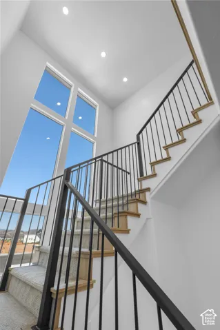 Staircase with wood treads and carpet runner, featuring black metal railings and large multi-pane windows
