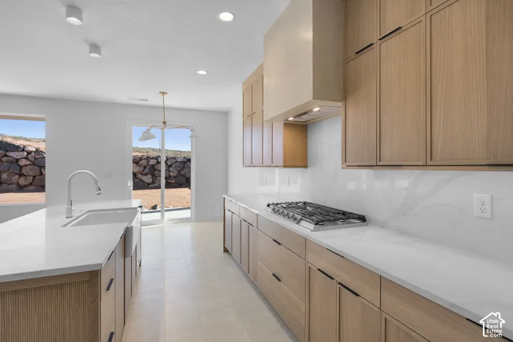 Modern kitchen featuring wood-finish cabinetry, white countertops, a built-in gas range, and a sleek range hood