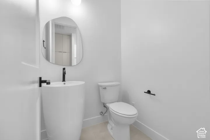 Pedestal basin with matte black faucet, wall-mounted mirror, and white toilet