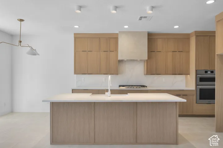 Kitchen featuring an island, light wood-finish cabinetry, a gas range with a built-in hood, double ovens, and recessed lighting