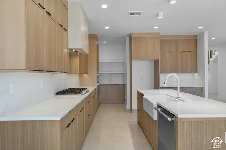 Modern kitchen featuring light wood-finish cabinetry, white countertops, a gas cooktop, a built-in range hood, and a farmhouse sink