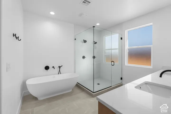 Freestanding soaking tub with matte black fixtures, glass-enclosed shower, single vanity with integrated sink and countertop, and light-toned tile flooring