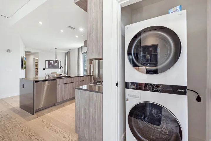 Integrated laundry appliances, light wood-finish flooring, recessed lighting, and a modern kitchen island with an undermount sink and stainless steel dishwasher