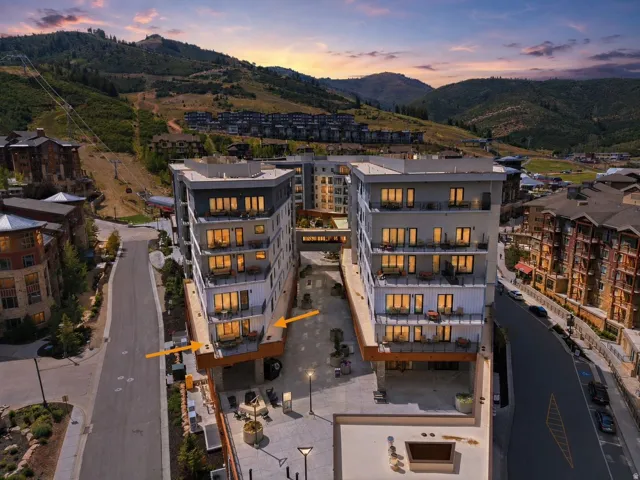 Modern multi-story buildings featuring balconies, a paved pedestrian area, and a surrounding mountainous landscape