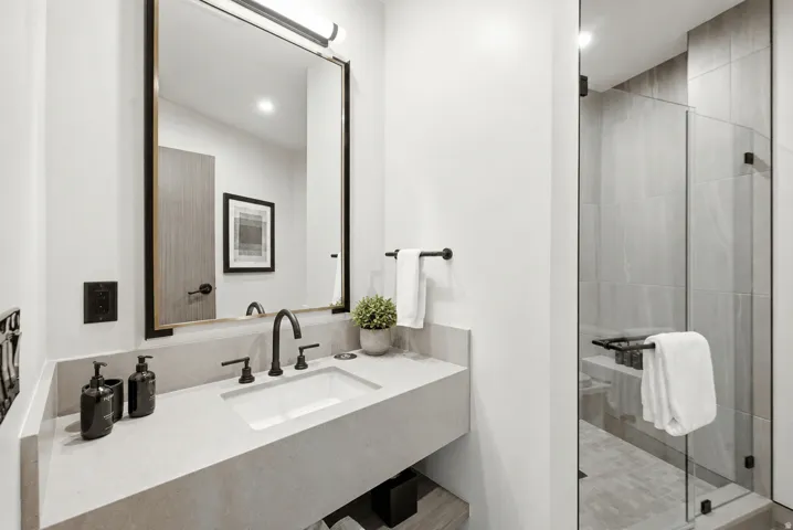 Floating vanity with integrated sink and matte black faucet, glass-enclosed shower with tile surround, and large framed mirror