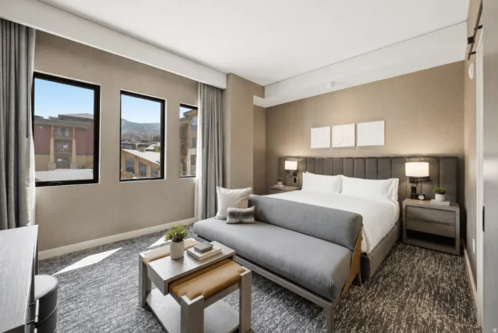 Contemporary hotel-style guest room featuring a king bed with upholstered headboard, dual nightstands with integrated lighting, and textured area rug