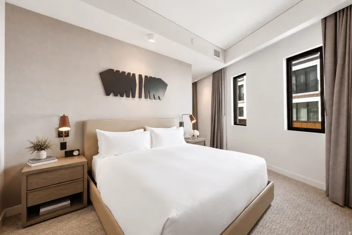Textured accent wall, recessed lighting, carpeted flooring, two dark-framed windows, and built-in bedside sconces