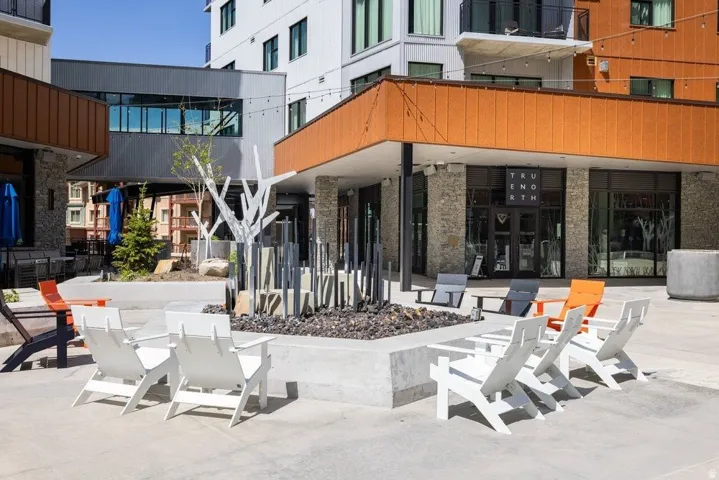 Expansive outdoor patio area featuring a concrete fire pit, decorative landscaping, and modern Adirondack-style seating