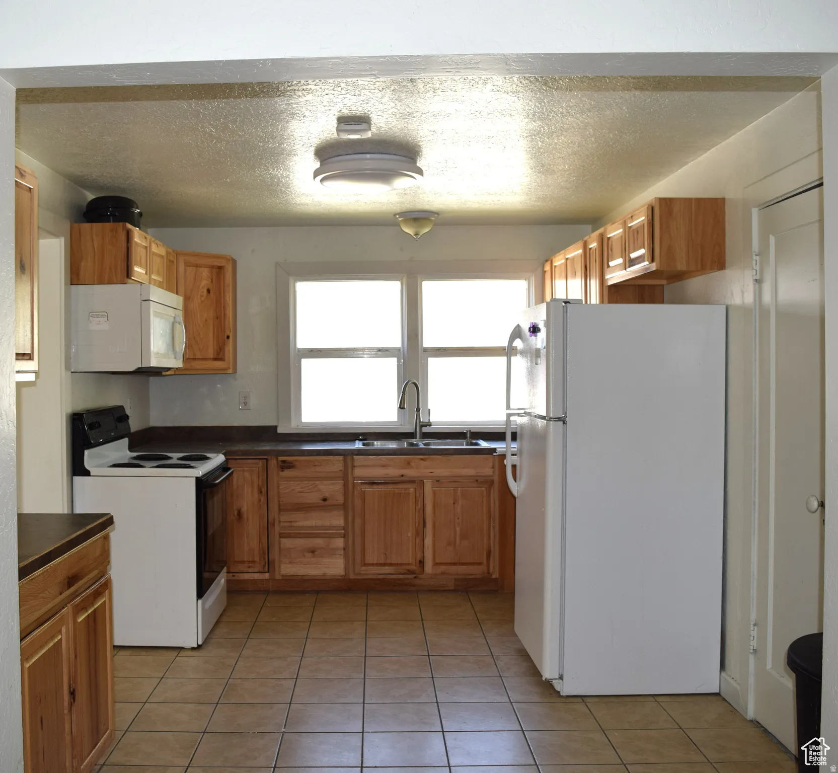 Kitchen featuring wood-finish cabinetry, tile flooring, white appliances, and a double basin sink with an arched faucet