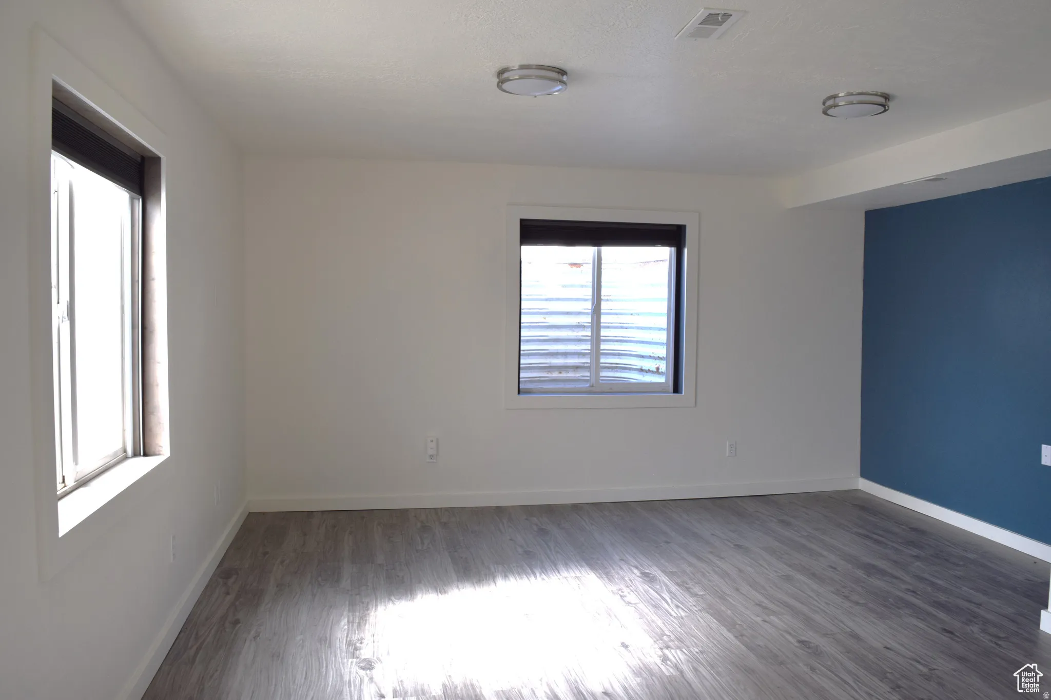 Spacious room featuring wood-finish flooring, white walls, and a single accent wall in blue