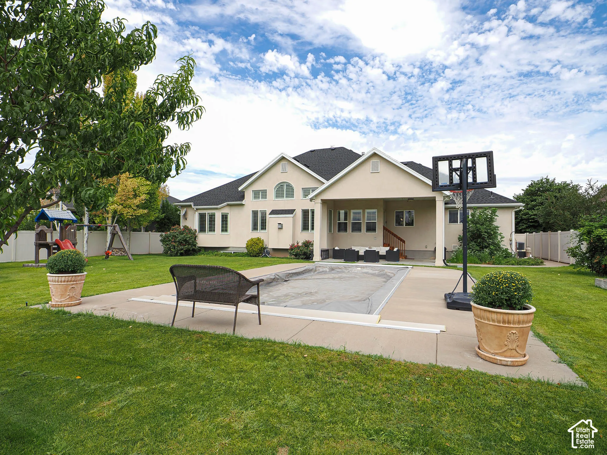 Spacious backyard featuring a covered swimming pool, concrete patio, expansive lawn, and mature landscaping