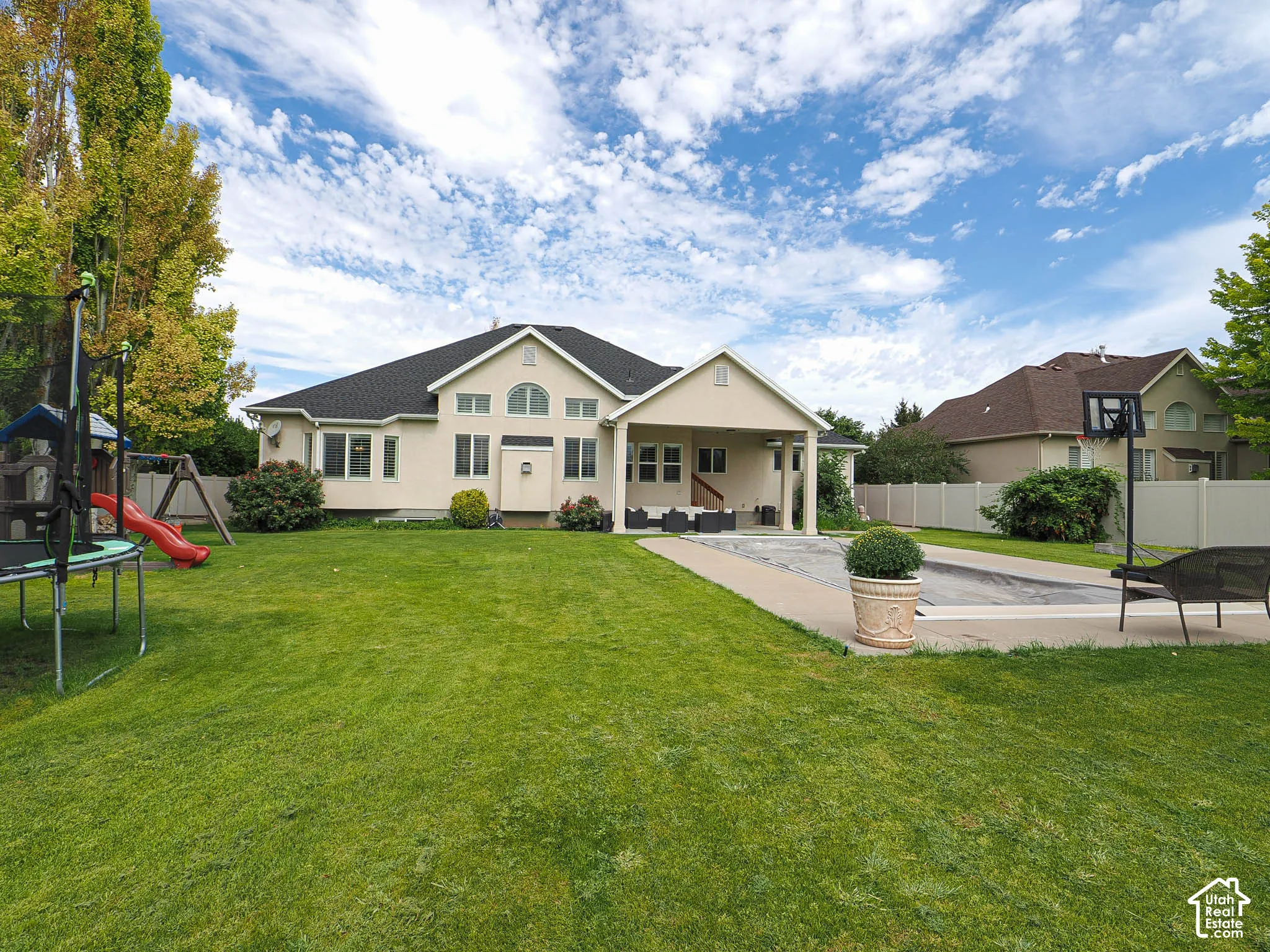 Expansive backyard featuring a large green lawn, covered patio, paved surround, and privacy fencing