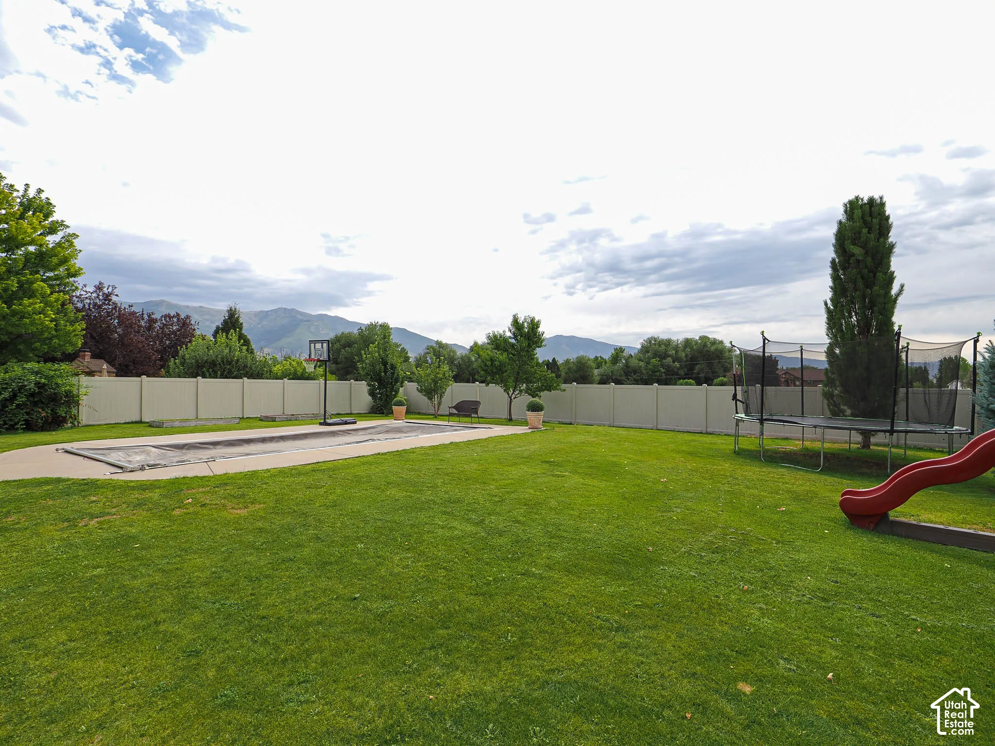 Expansive backyard featuring a manicured lawn, established perimeter fencing, and a hardscaped patio area