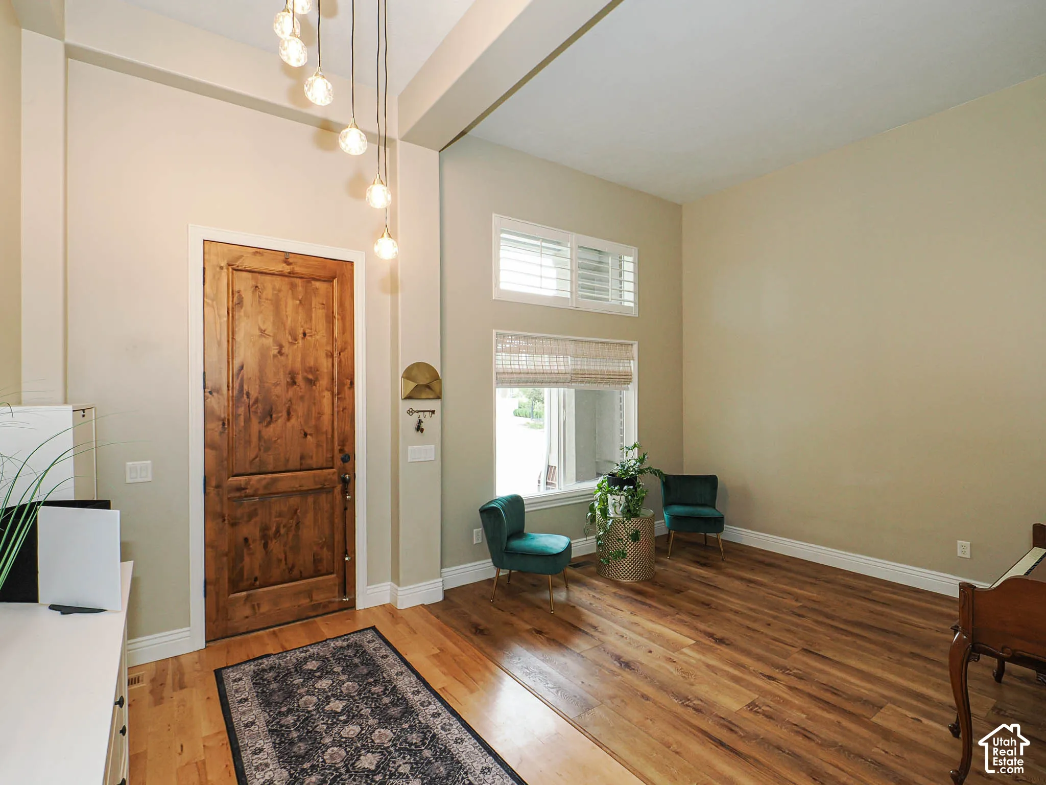 Wood-finish flooring, high ceilings, natural wood door, multi-pane windows with plantation shutters, and a suspended lighting fixture