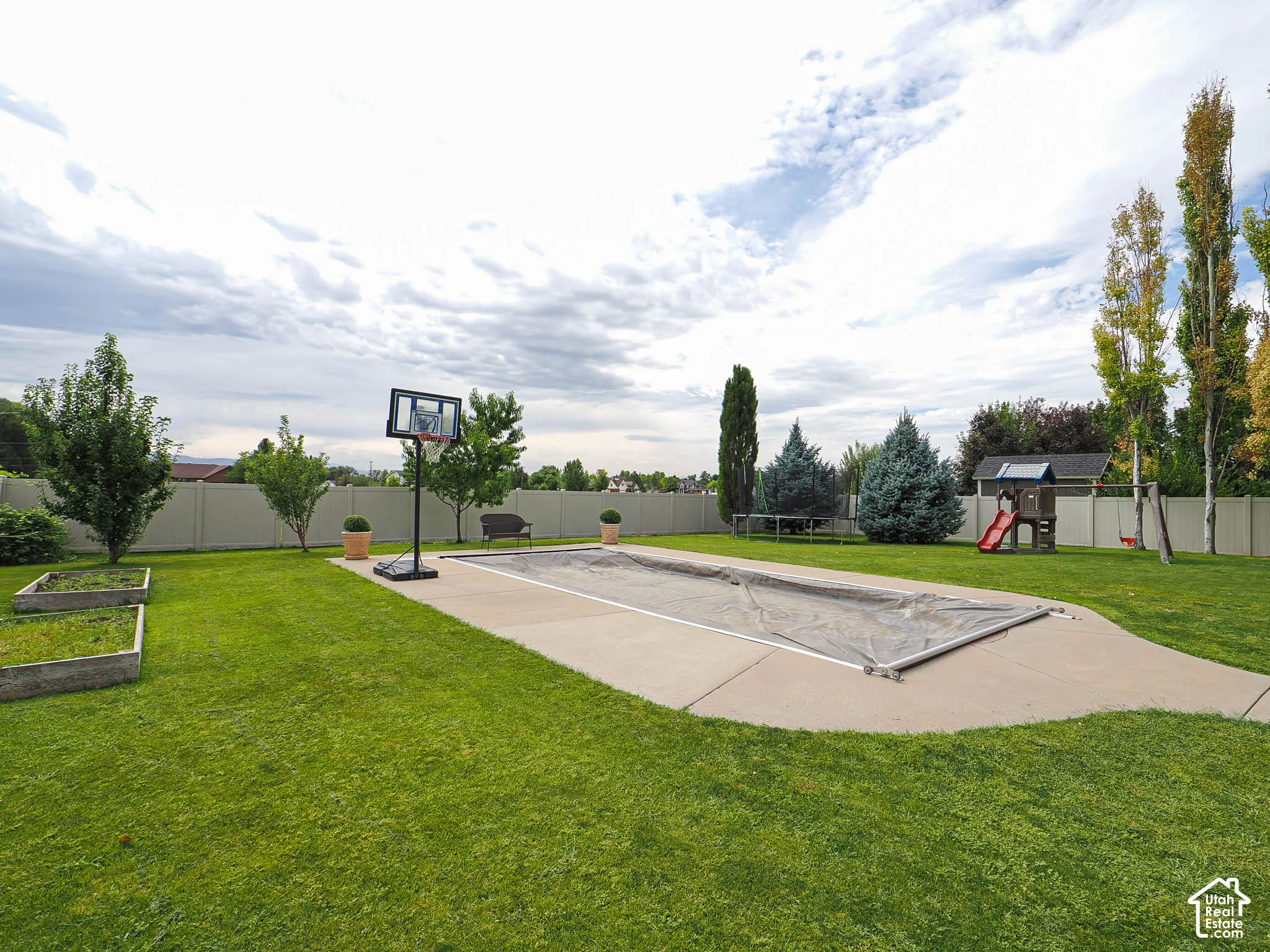 Expansive green lawn with a covered in-ground pool, concrete surround, and perimeter fencing