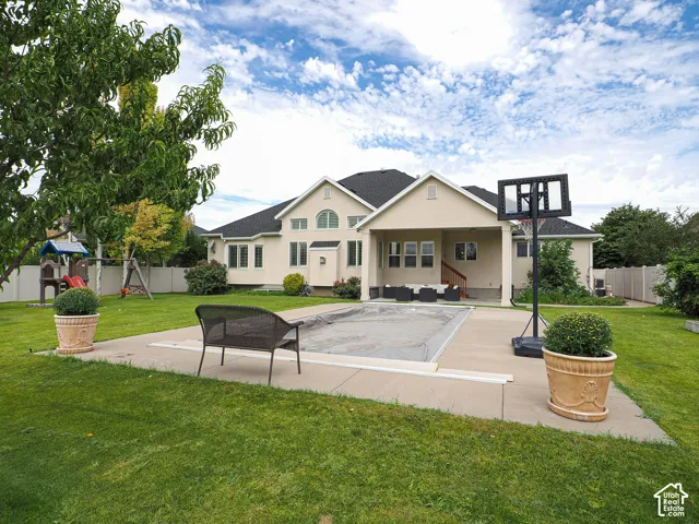 Spacious backyard featuring a covered swimming pool, concrete patio, expansive lawn, and mature landscaping