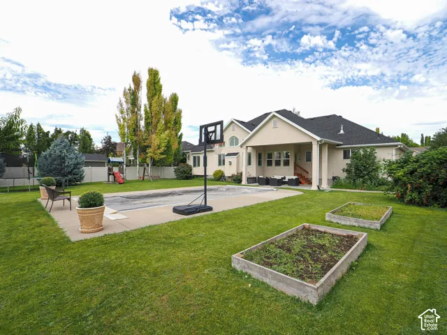 Expansive backyard featuring a covered patio, concrete pool deck, and raised garden beds
