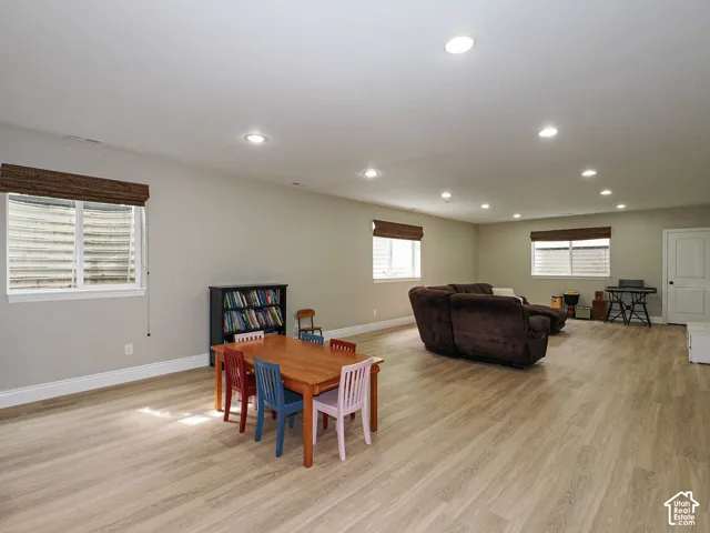 Spacious room featuring light wood-finish flooring, recessed lighting, multiple windows with blinds, and painted walls