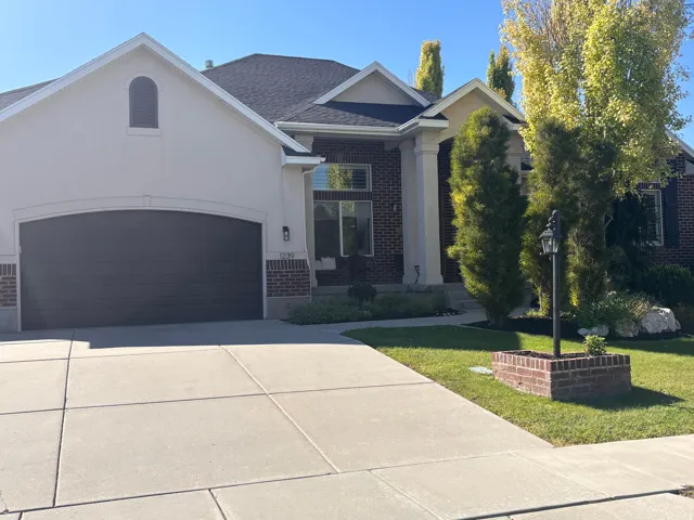 Stucco and brick exterior with a dark garage door, concrete driveway, manicured lawn, and established landscaping