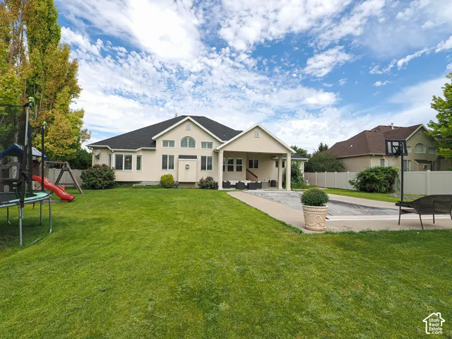 Expansive backyard featuring a large green lawn, covered patio, paved surround, and privacy fencing