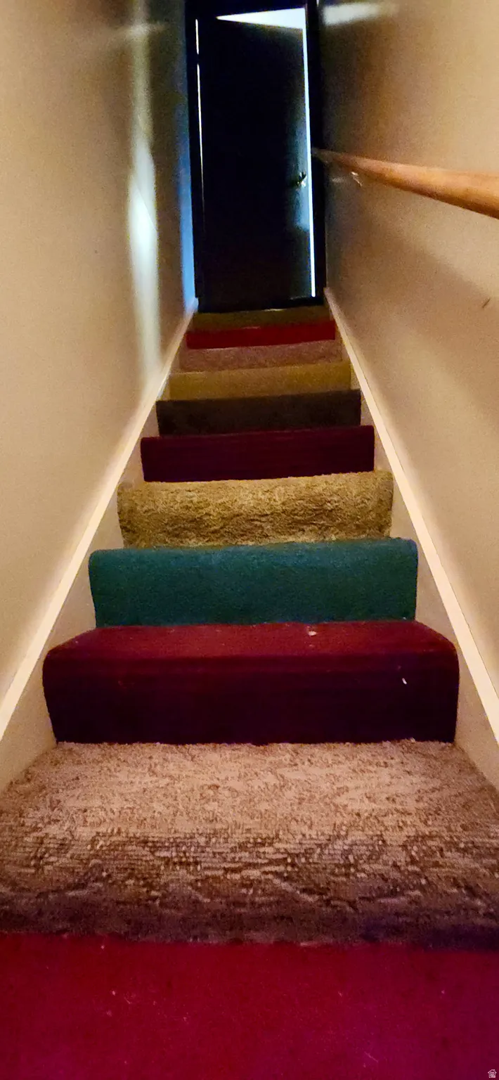 Staircase featuring colorful carpeted treads and a wooden handrail