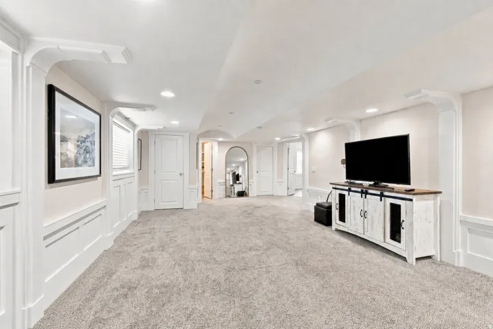 Recessed lighting illumination, wall paneling, carpet flooring, arched doorway, and built-in architectural pillars