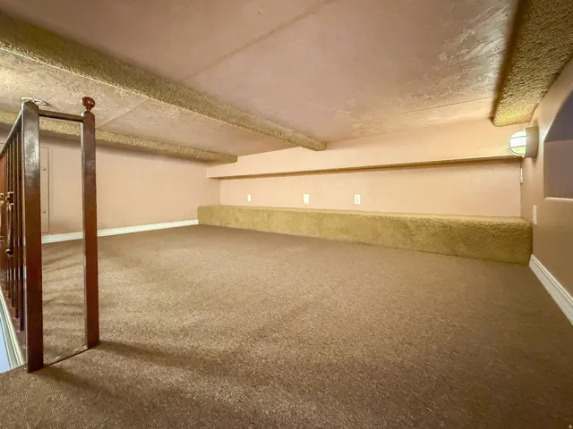 Loft area featuring carpeting, wood railing, built-in shelving, and a wall-mounted light fixture