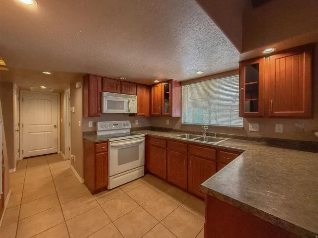 Kitchen featuring wood-finish cabinetry, tile flooring, recessed lighting, double basin sink, and white appliances