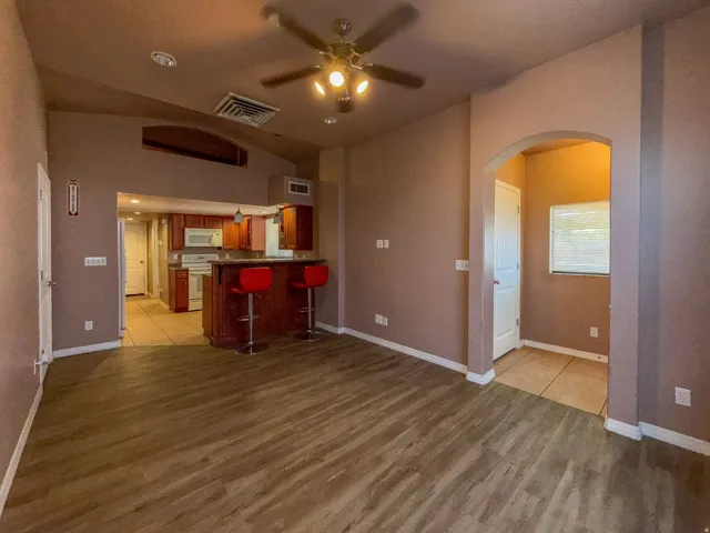Vaulted ceiling with an illuminated ceiling fan, wood-finish flooring, arched entryway, and kitchen with a breakfast bar