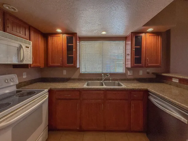 Wood-finish cabinetry with glass-front accents, dual basin stainless steel sink, solid surface countertops, and recessed lighting