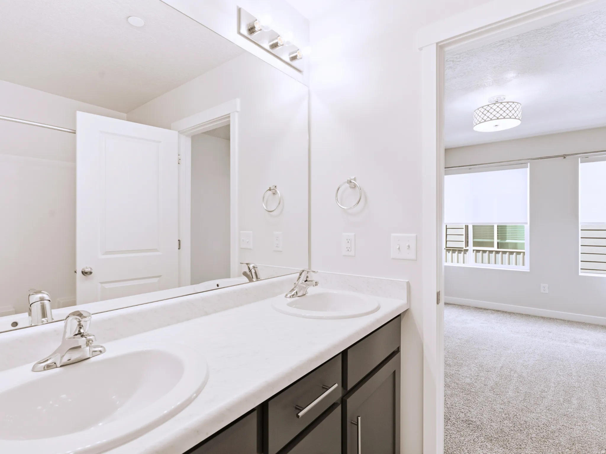 Dual vanity with integrated sinks, chrome faucets, black cabinetry, and a full-width mirror