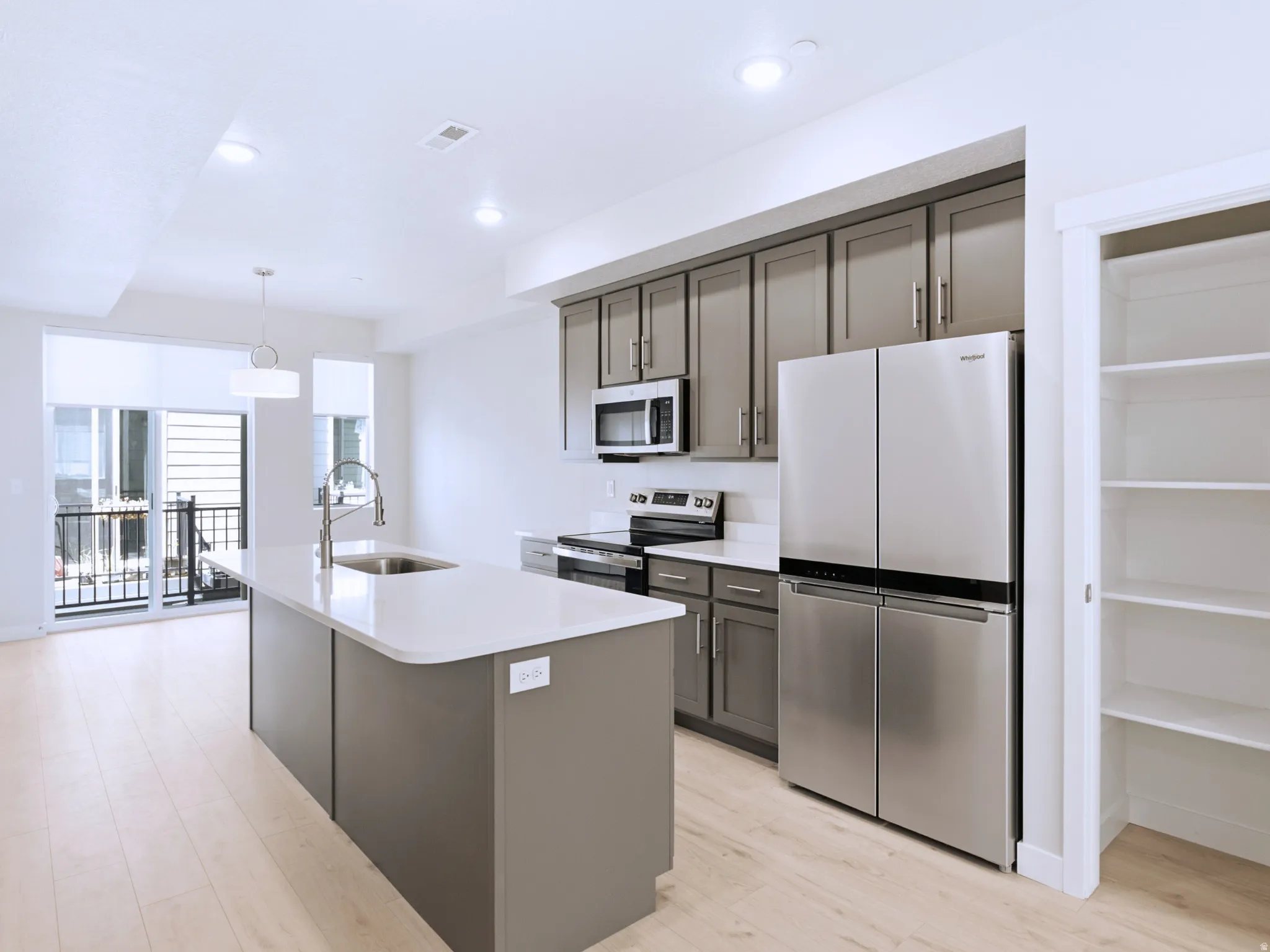Kitchen featuring a center island with sink, stainless steel appliances, grey cabinetry, and light wood-finish flooring