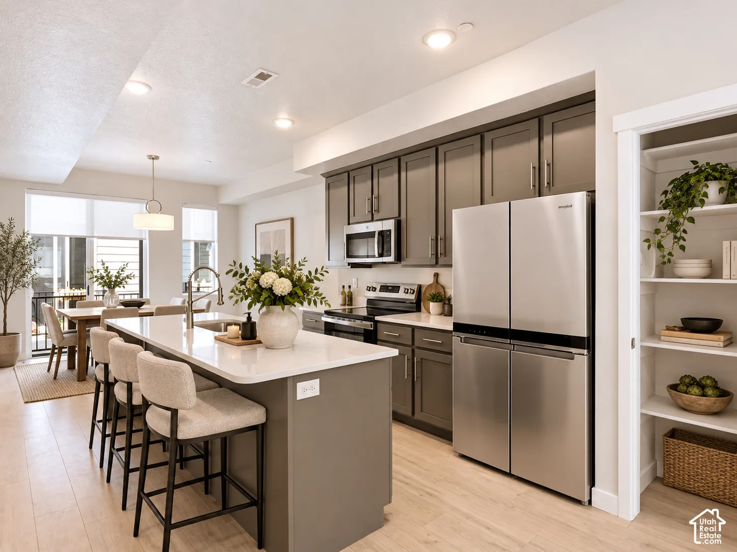 Kitchen featuring matte-finish cabinetry, quartz countertops, stainless steel appliances, a center island with an undermount sink, and a walk-in pantry with built-in shelving