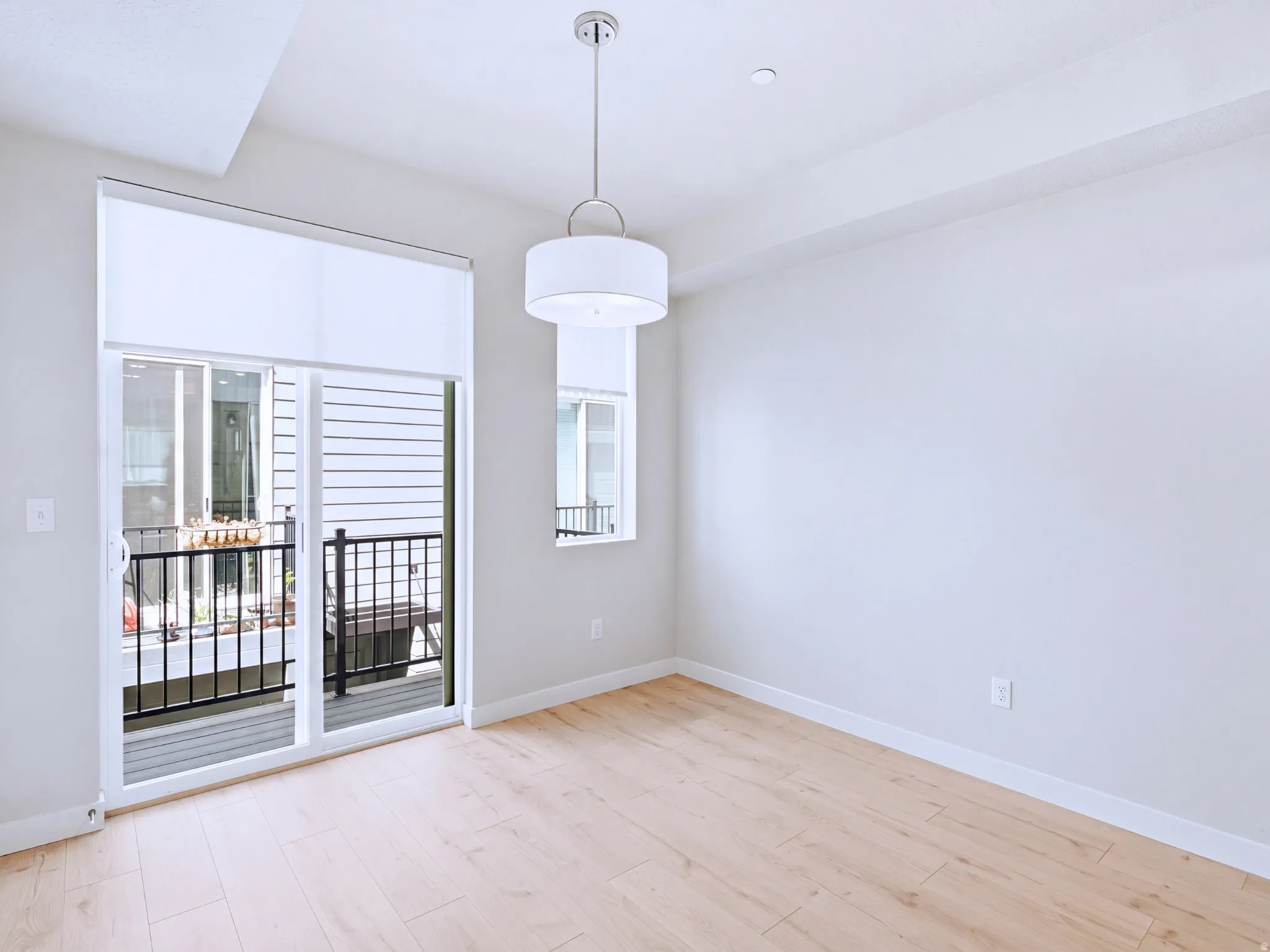Bright corner bedroom featuring light wood-finish flooring, white walls, and abundant natural light from French doors opening to a private balcony
