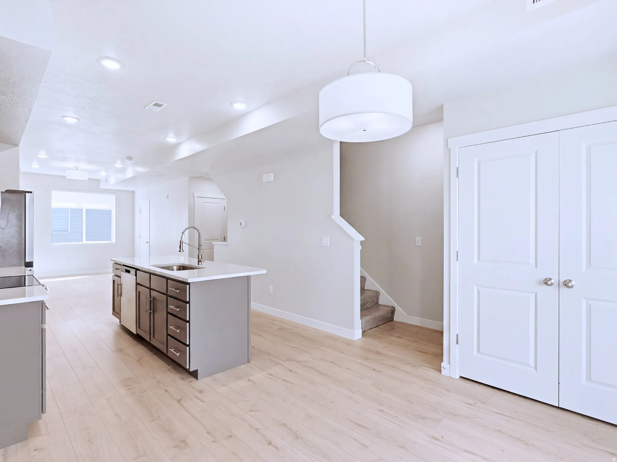Kitchen island with integrated sink, stainless steel appliances, wood-finish flooring, recessed lighting, and a contemporary drum pendant light fixture