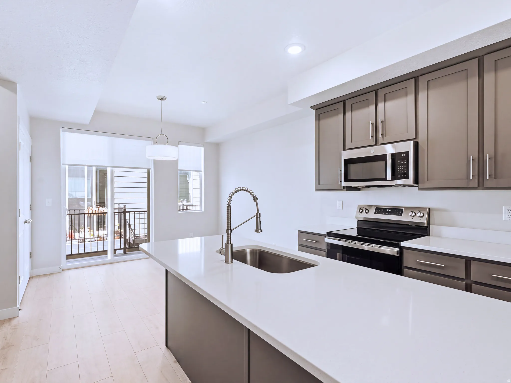 Kitchen featuring an island with an undermount sink, stainless steel appliances, grey cabinetry, and wood-finish flooring